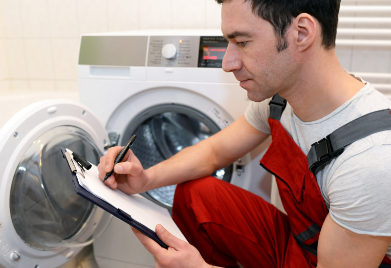 Monteur macht sich Notizen zu einer defekten Waschmaschine