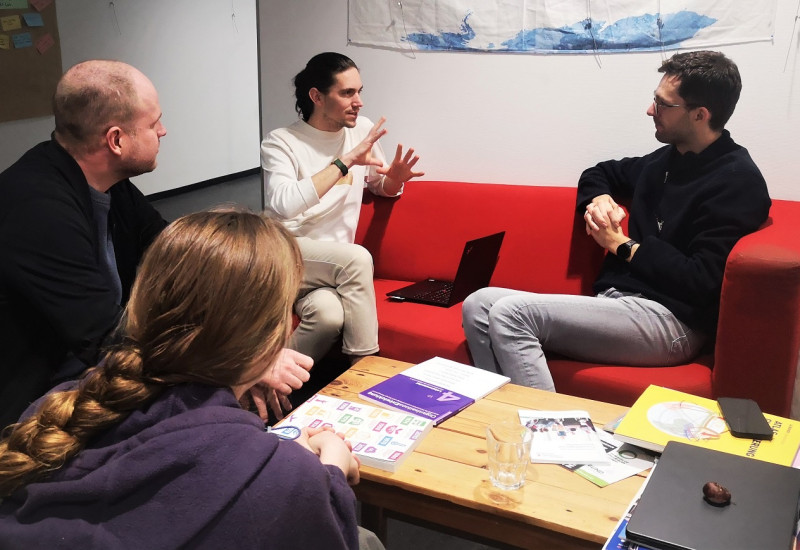 drei Männer und eine Frau sitzen um einen Tisch und diskutieren Fragestellungen