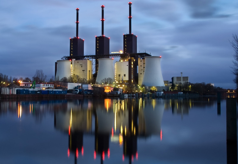 Energiekraftwerk bei Nacht, die Beleuchtung der hohen Schornsteine spiegelt sich im Wasser.