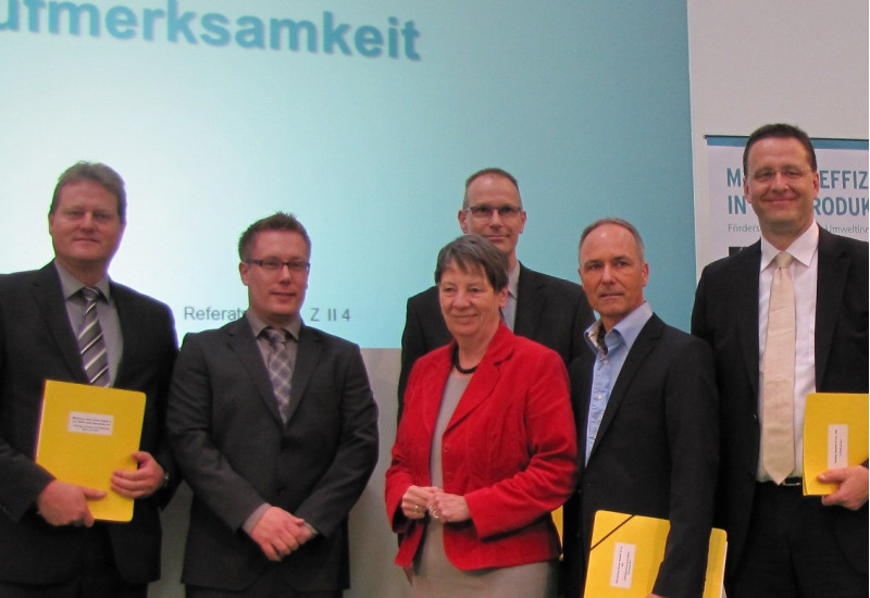 Bundesumweltministerin Hendricks und fünf Herren in Anzügen stehen lächelnd auf einer Bühne, drei Herren haben gelbe Mappen unter dem Arm, im Hintergrund ein Plakat zum Umweltinnovationsprogramm