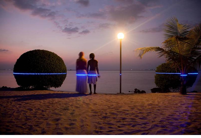Ein Pärchen steht am Strand blickt in den Sonnenuntergang über dem Meer. In Hüfthöhe zeigt ein blauer Laser, wie hoch Ihnen das Wasser stehen könnte. 