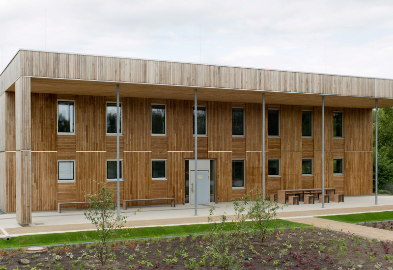 zweistöckiges, quadratisches Haus mit Flachdach und Holzfassade, davor sind Außenanlagen frisch bepflanzt und Wege neu angelegt