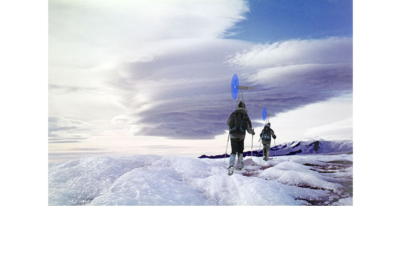 Zwei Bergsteiger laufen auf Schneeschuhen durch eine Eislandschaft, auf dem Rücktragen tragen sie mobile Windräder und erzeugen Strom
