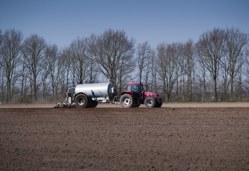 a tractor with trailer spreads slurry on a field