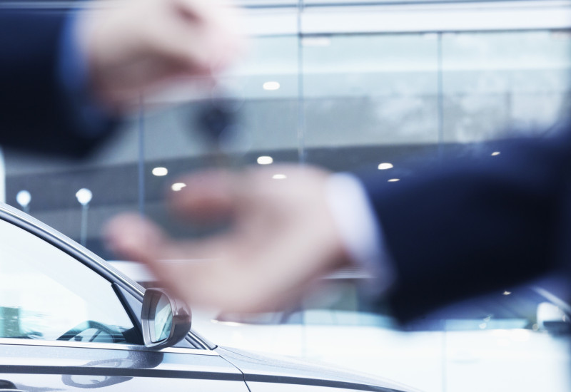 Übergabe des Autoschlüssels, im Hintergrund das Auto