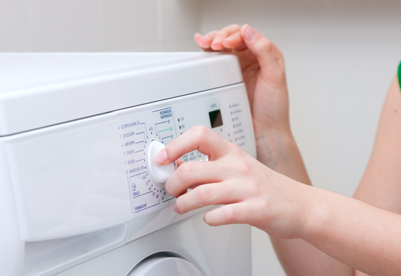 Eine Frau dreht am Programmwählknopf einer Waschmaschine.