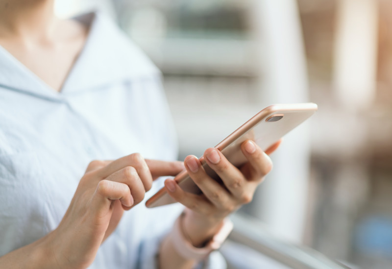 Eine Frau hält ein Smartphone in der Hand und tippt mit der anderen Hand darauf