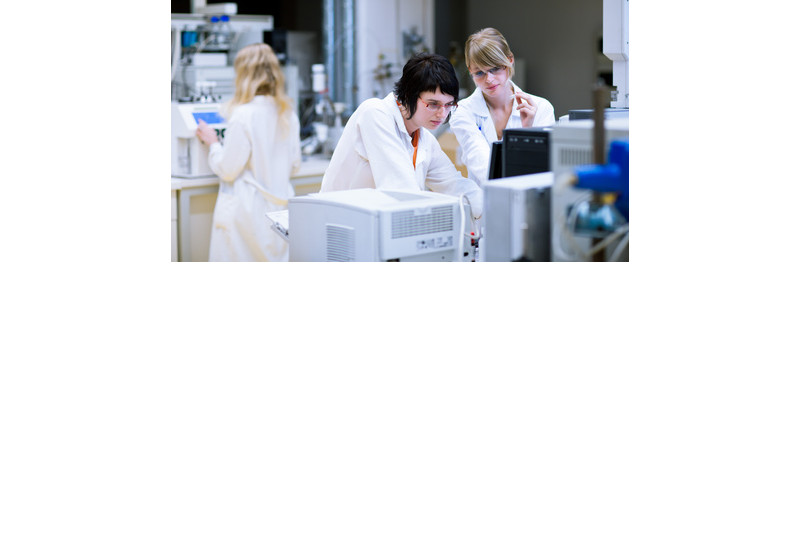 Drei Wissenschaftlerinnen in Laborkitteln arbeiten in einem modernen Analyselabor.