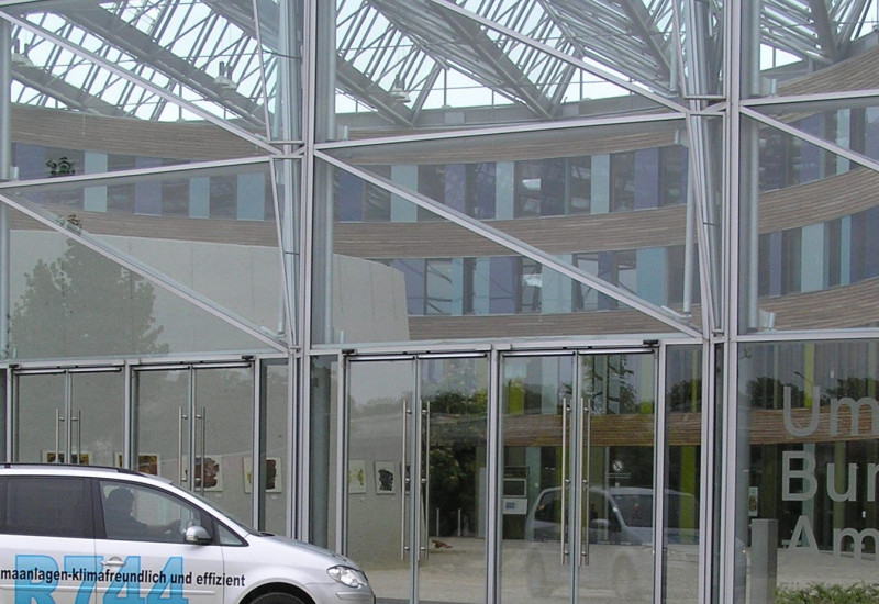 Ein silberner VW Touran steht vor Glastüren. Auf dem Auto steht in scharzer Schrift: CO2-Klimaanlagen - klimafreundlich und effizient 
