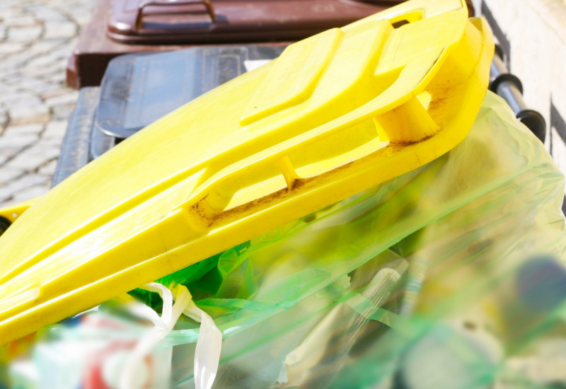 Eine gelbe Mülltonne mit einer Plastiktüte voller Verpackungsmüll.