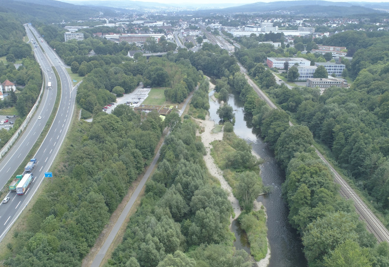 Ein renaturierter Fluss in der Mitte, links eine Autobahn, rechts Bahngleise.