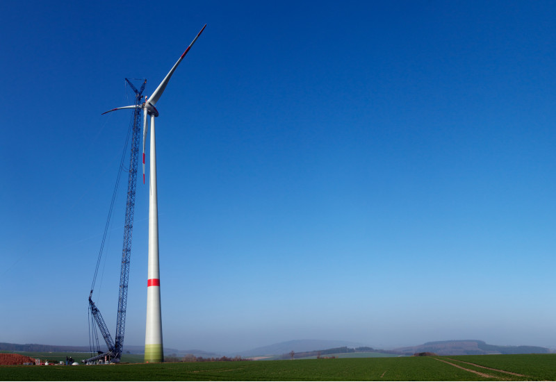 Eine Windkraftanlage in der Konstruktion vor blauem Himmel mit einem großen Kran.