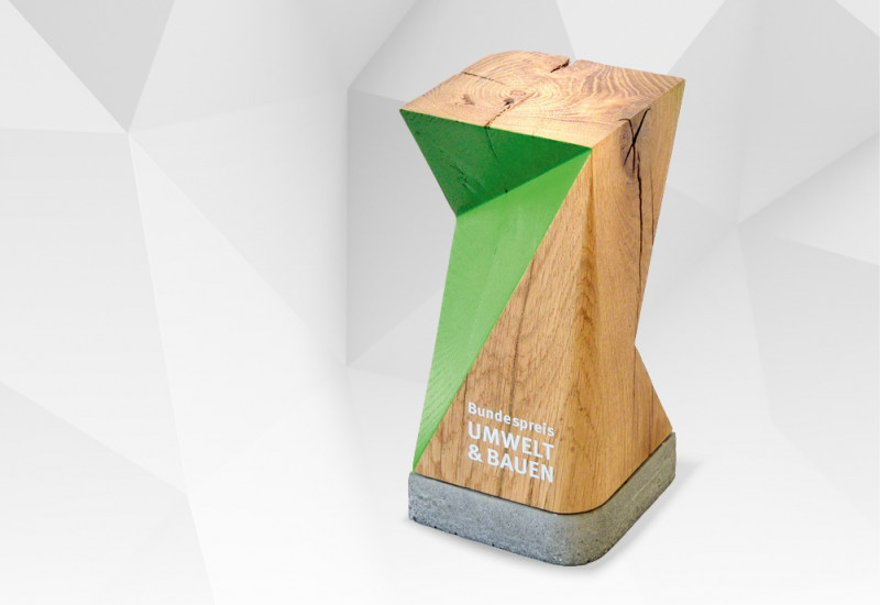 Schriftzug "Bundespreis Umwelt & Bauen" und Bild einer Trophäe aus Holz