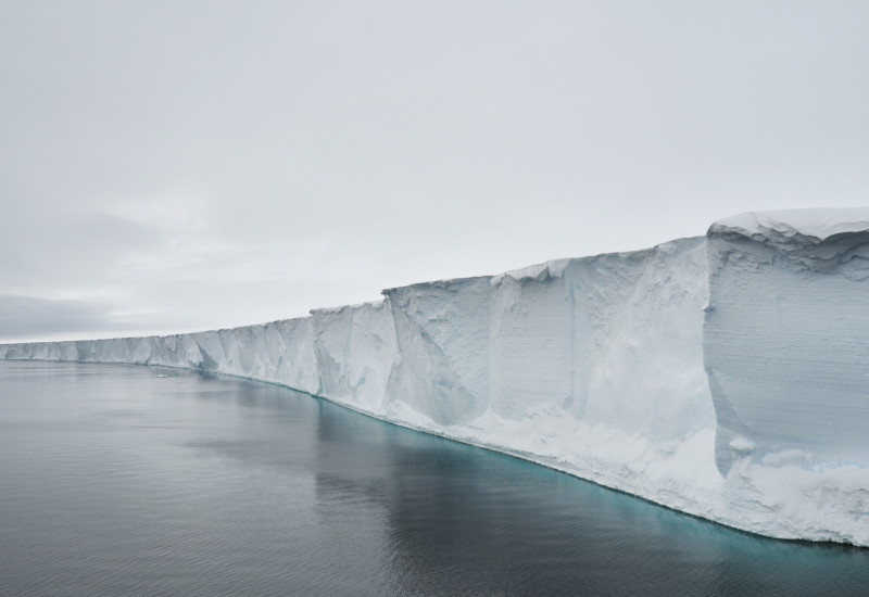 Enormous ice shelves float on the ocean, connected to a glacier onshore.