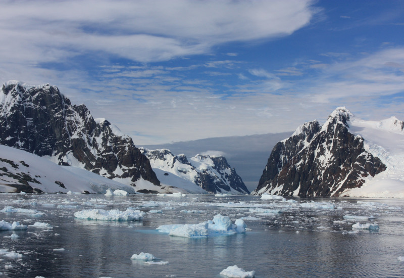Das Bild zeigt eine Bucht in der Antarktis. Auf dem dunklen Wasser schwimmen Eisschollen. Im Hintergrund begrenzen Berge die Bucht. 