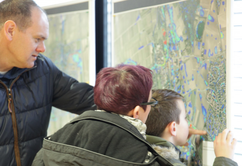 Familie schaut sich eine Landkarte an und der Vater zeigt seinem Sohn und seiner Ehefrau etwas auf der Karte, die aus der Luft fotografiert wurde und farbig markierte Bereiche hat