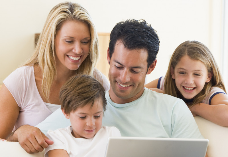 Familie sitzt auf dem Sofa und schaut zusammen auf den geöffneten Laptop