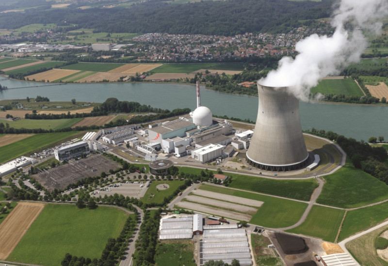 Das Bild zeigt das Luftbild eines Kernkraftwerks mit einem Wasserdampf absondernden Kühlturm am Rande eines Flusses.