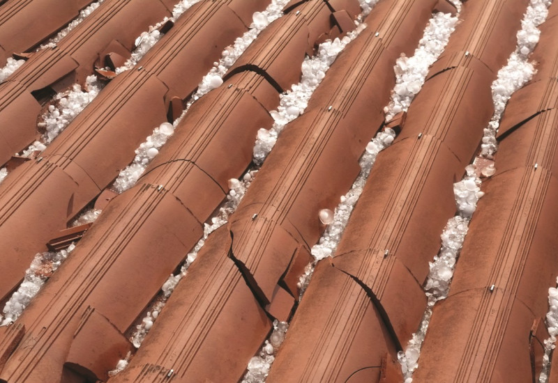 The picture shows a tiled roof surface covered with and destroyed by hailstones. 