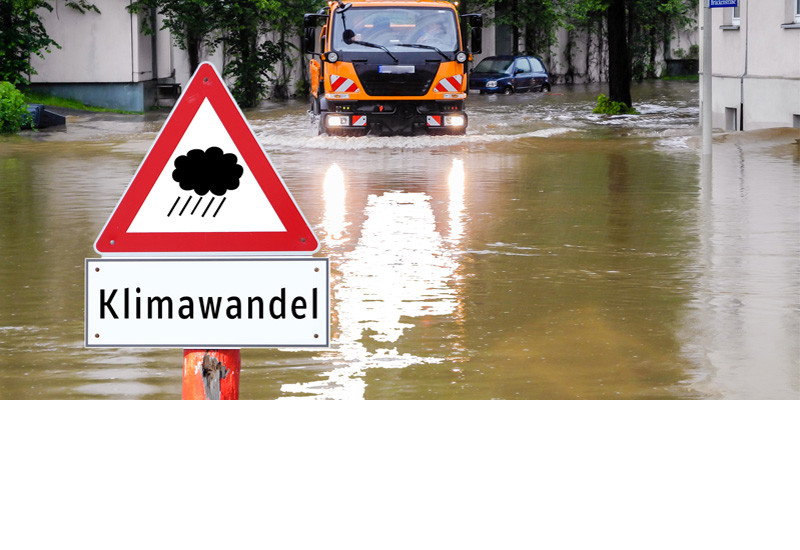 von Starkregen überflutete Straße mit Warnschild "Klimawandel"