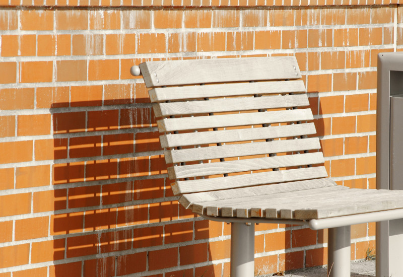 Das Bild zeigt eine Bank aus unbehandeltem Holz mit einem Unterbau aus Metall, der verhindert, dass das Holz Bodenkontakt hat.