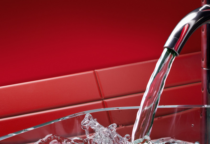 Laufender Küchenwasserhahn mit Glasschale, roter Hintergrund