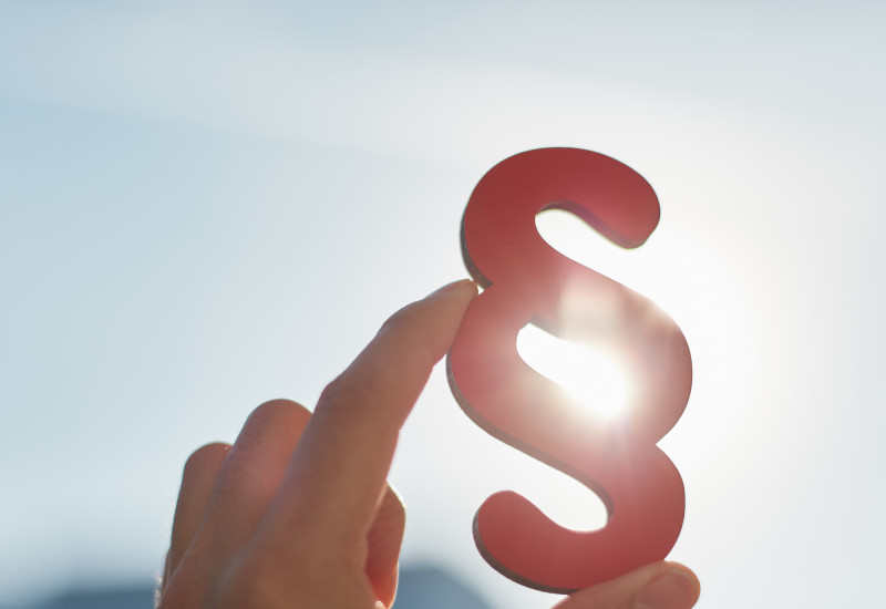 ParagrafenSymbol wird in der Hand halten, vor einem Himmel. Es scheint die Sonne.