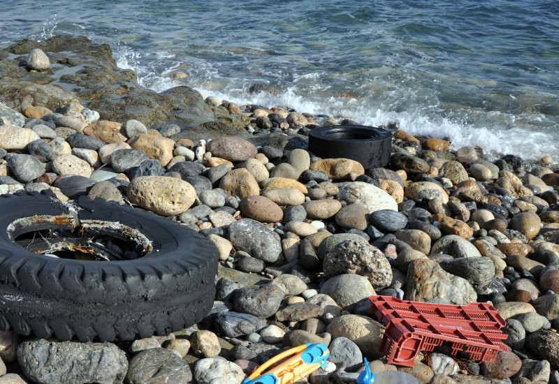 Plastikreste am Meer: Ein alter Reifen, eine Flasche, Kinderspielzeug und der Rest eines Einkaufkorbs aus Plastik liegen auf einem Kiesstrand.