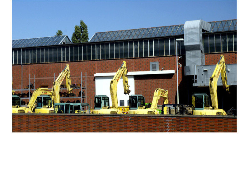 Sieben Bagger stehen auf einer Gewerbefläche vor einer Industriehalle