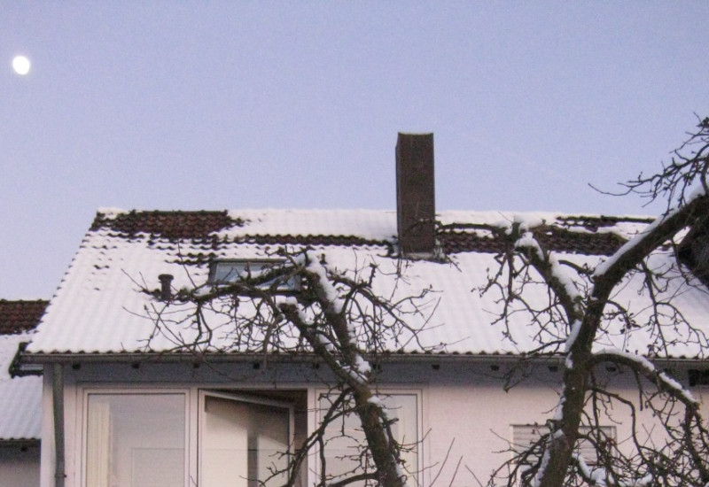 Ein zweistöckiges Reihenhaus mit Terrasse und Balkon in verschneitem Garten.