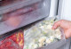 Eine Hand holt eine Plastiktüte mit gefrorenen Zucchini-Stücken aus dem Gefrierfach eines Kühlschranks. Im Fach darunter befinden sich Tüten mit anderen gefrorenen Lebensmitteln, wie zum Beispiel Paprika.