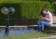 Eine Frau sitzt in einem Park auf einer Bank, trägt einen Mund-Nasen-Schutz und schaut auf ihr Smartphone
