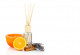 eine orange Duftkerze, ein Aromafläschchen mit Holzstäbchen zur Raumluft-Beduftung, eine halbe Orange, ein Lavendelsträußchen und Zimtstangen