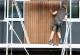 zwei Bauarbeiter stehen auf einem Baugerüst und montieren zusammen ein Holz-Fassadenelement