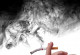 Hand hält eine schon halb zu Asche gewordene Zigarette, von der schwarzer Qualm aufsteigt