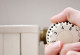 Nahaufnahme: Eine Hand dreht das Thermostat einer Heizung auf.