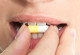 Das Bild zeigt den Mund einer Frau. Mit ihrer rechten Hand führt sie eine Tablette an ihren Mund. 