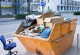Ein Müllcontainer steht auf der Straße, daneben steht ein Bürostuhl