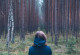 Frau steht mit Rücken zugewandt im Wald.