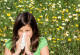 A girl blows her nose. In the background is a flower meadow with daisies an dandelion.