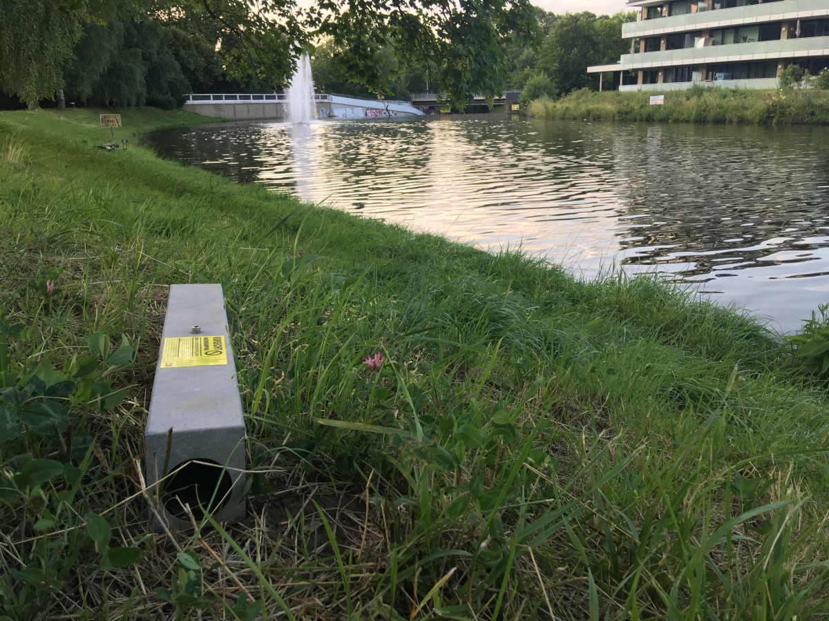 Köderstation mit Warnhinweis vor Rattengift steht am Uferbereich eines Flusses