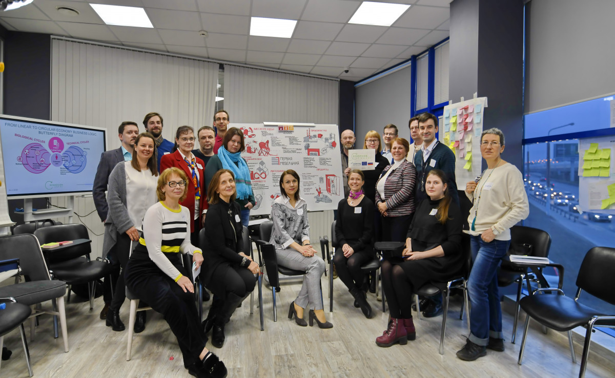 Eine Gruppe von Menschen sitzt bzw. steht vor einem Flipchart.