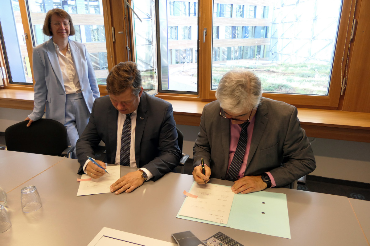 Herr Prof. Dr. Krabbes und Herr Dr. Scheremt unterzeichnen die Vereinbarung am Tisch, Frau Dr. Ranft steht links am Tisch