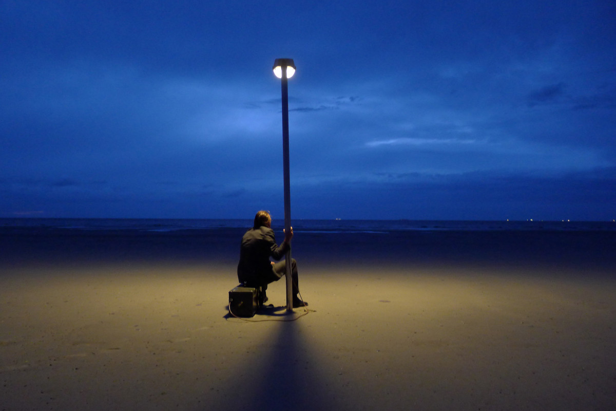 Mann sitzt zur blauen Stunde mit seiner leuchtenden Laterne am Strand.