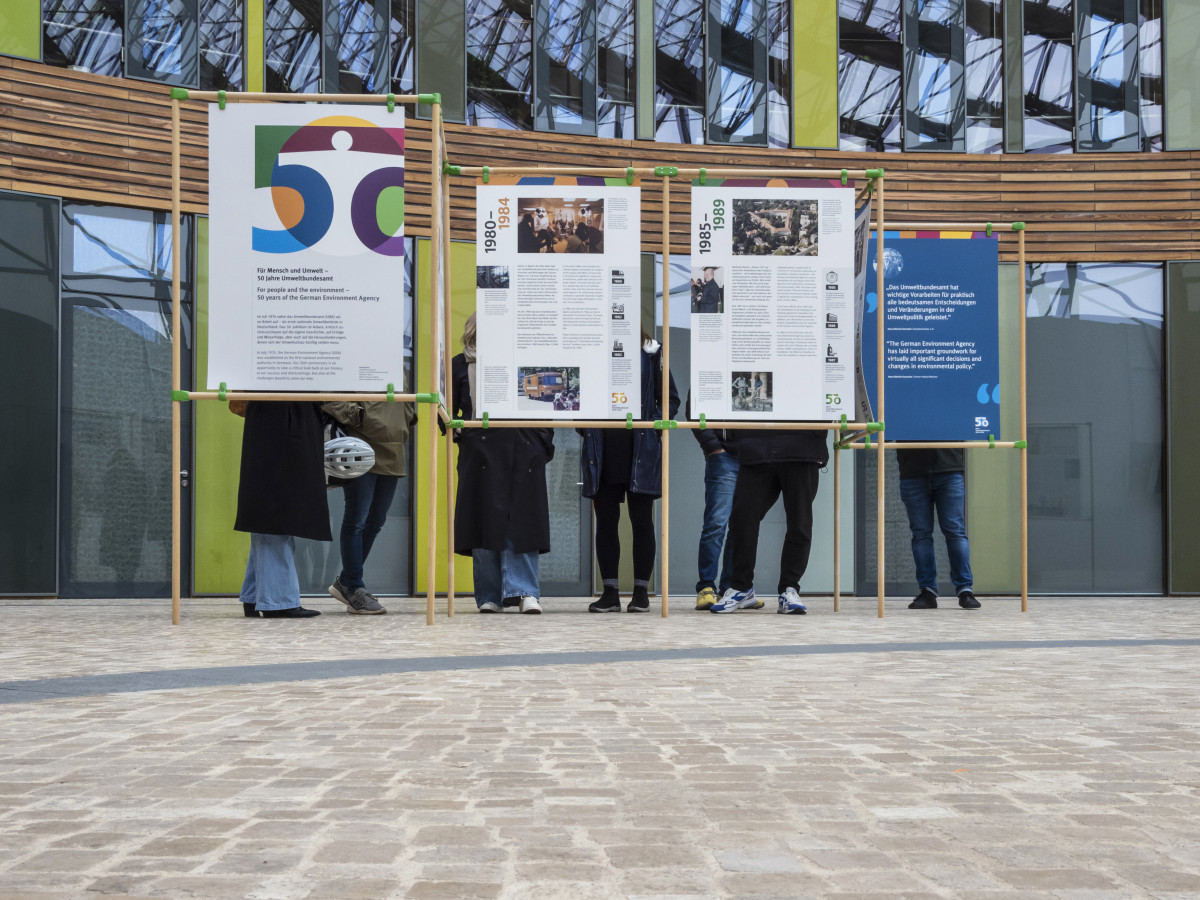 Foto mit den neuen UBA-Ausstellungstalfen in Dessau-Roßlau. Zu sehen ist ein Teil der Ausstellung mit Menschen hinter den Tafeln. 