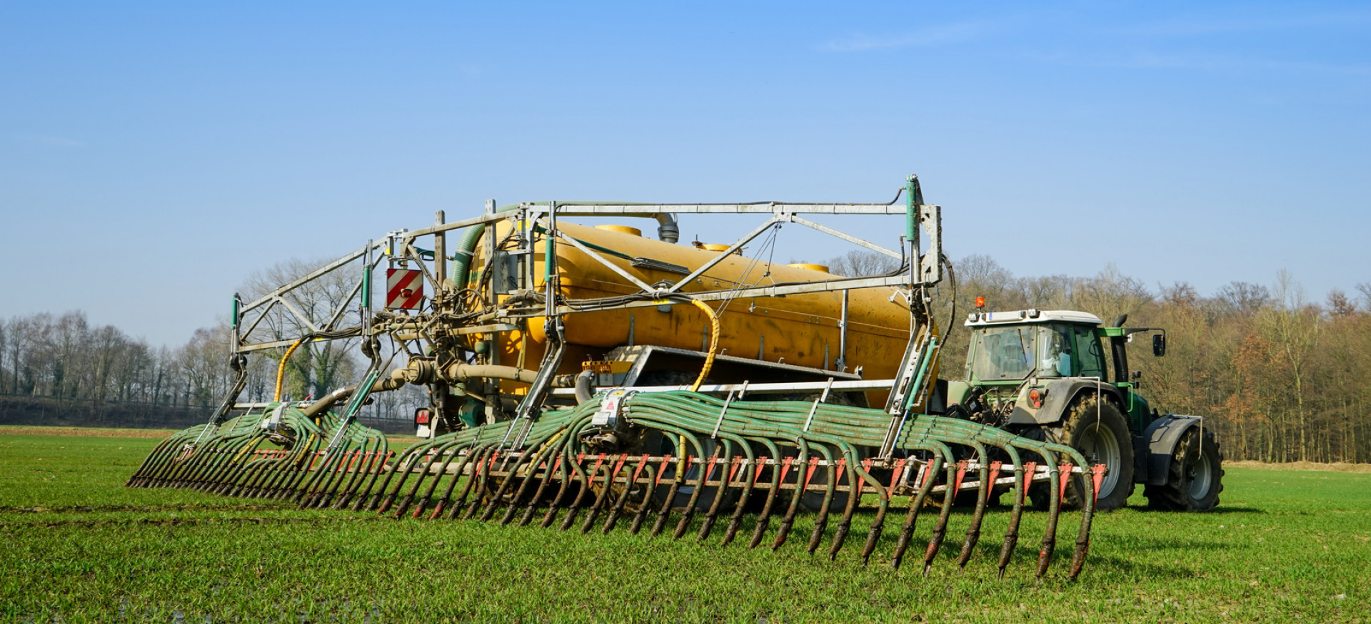 Traktor mit Gülletank und Schleppschlauch auf landwirtschaftlicher Nutzfläche 