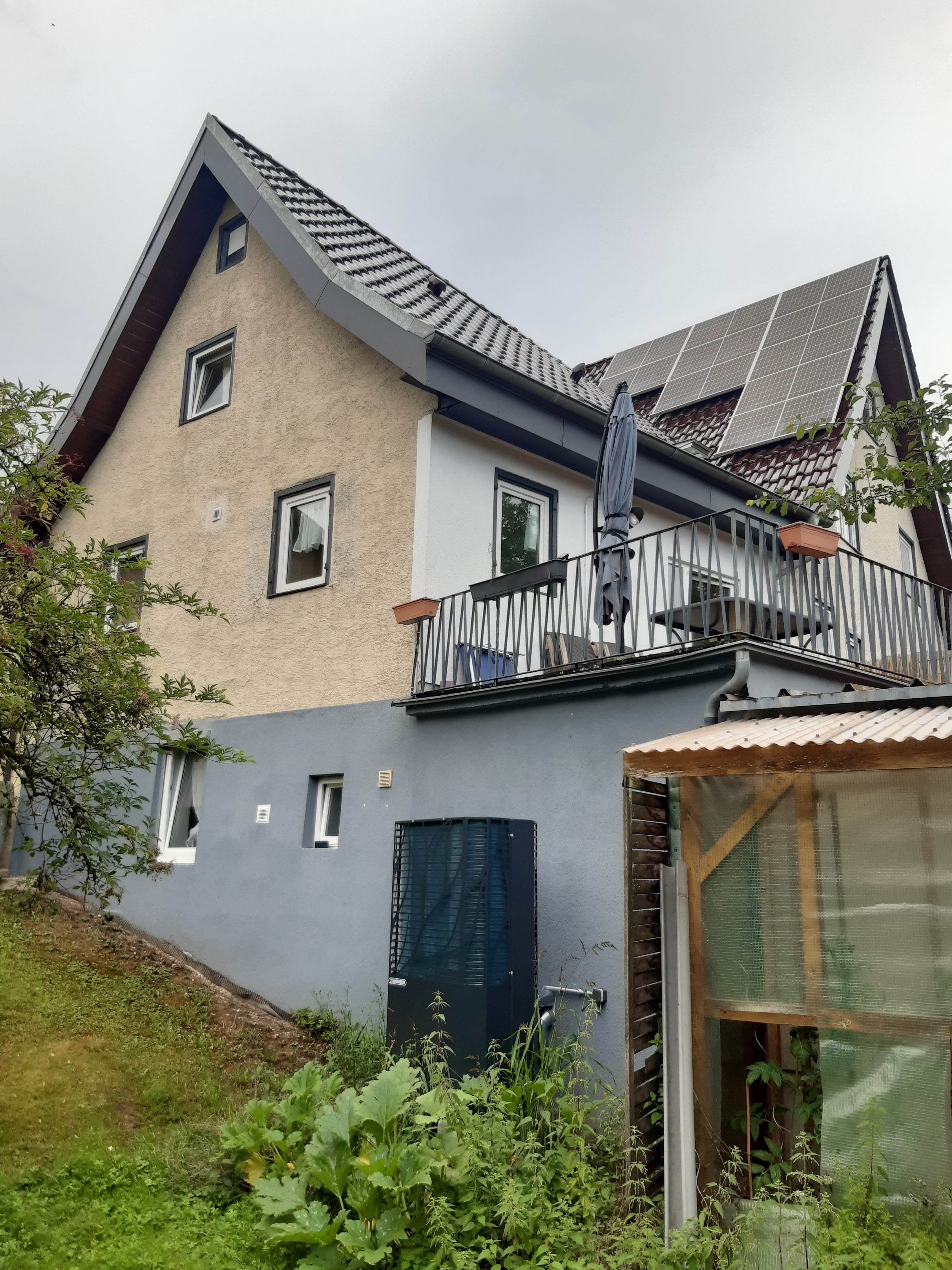 Einfamilienhaus mit Satteldach, auf dem Solarpaneele installiert sind, und einer Wärmepumpe neben dem Haus im Gartenbereich