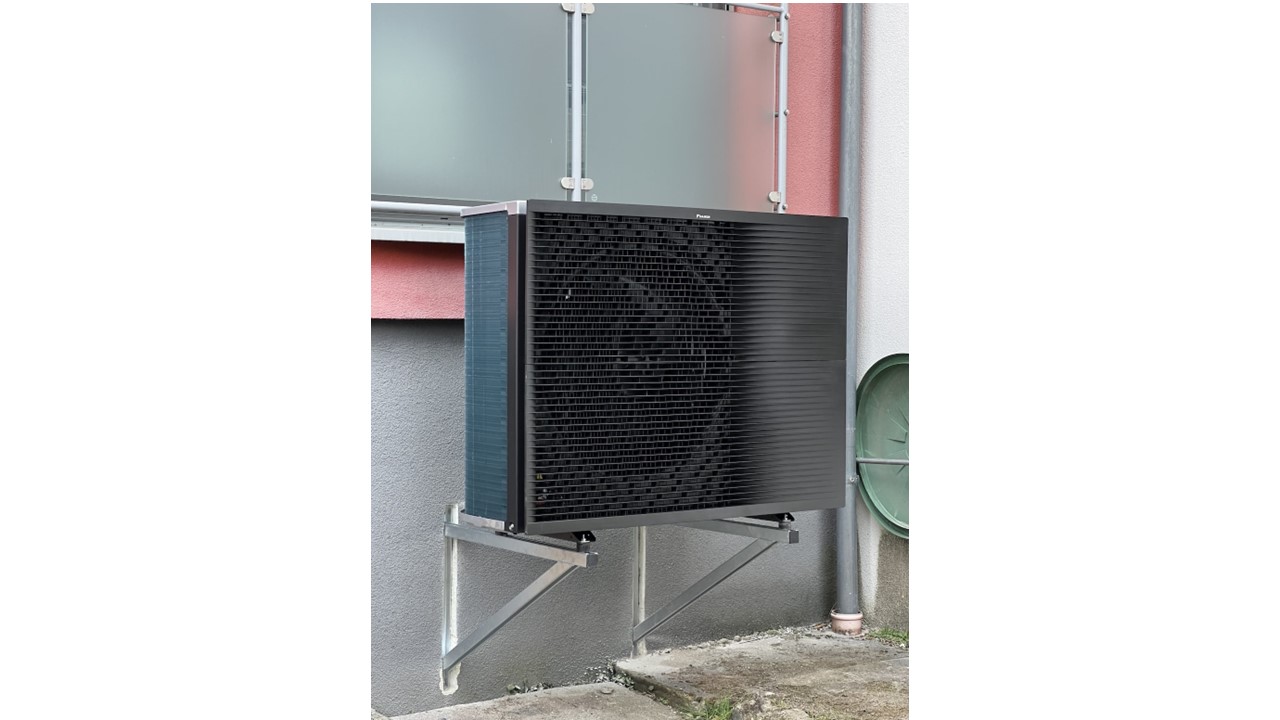 Die Außeneinheit einer Wärmepumpe vor einer Balkonbrüstung.