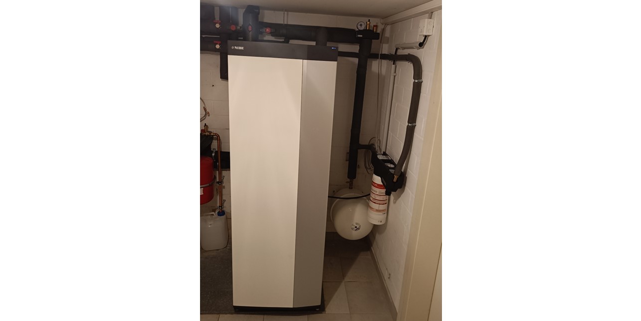 Die Erdwärmepumpe im Heizungskeller ist ein schmaler, fast raumhoher Metallquader. Daneben sind isolierte Anschlussleitungen zu sehen.