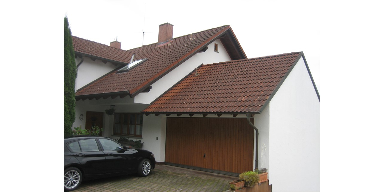 Doppelhaushälfte von der Straßenseite aus gesehen; im Vordergrund die Garage mit Auto in der Einfahrt